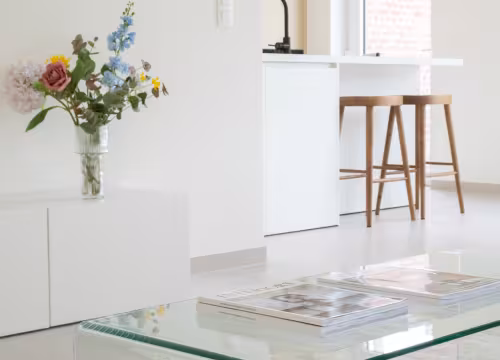 Interieurdetail van leefruimte met glazen salontafel en zicht op moderne keuken